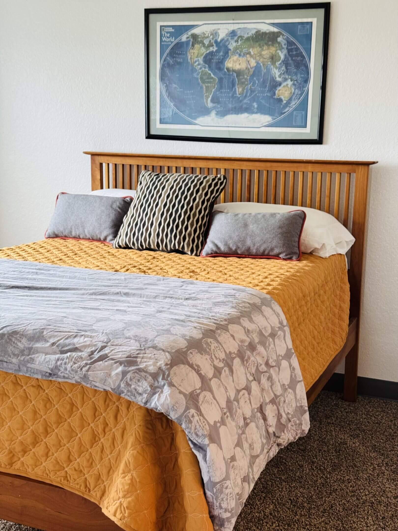 Neatly made bed with a mustard yellow quilt and patterned gray blanket.