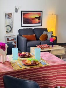 Cozy living room with a dark sofa, colorful cushions, and a vibrant table setting.